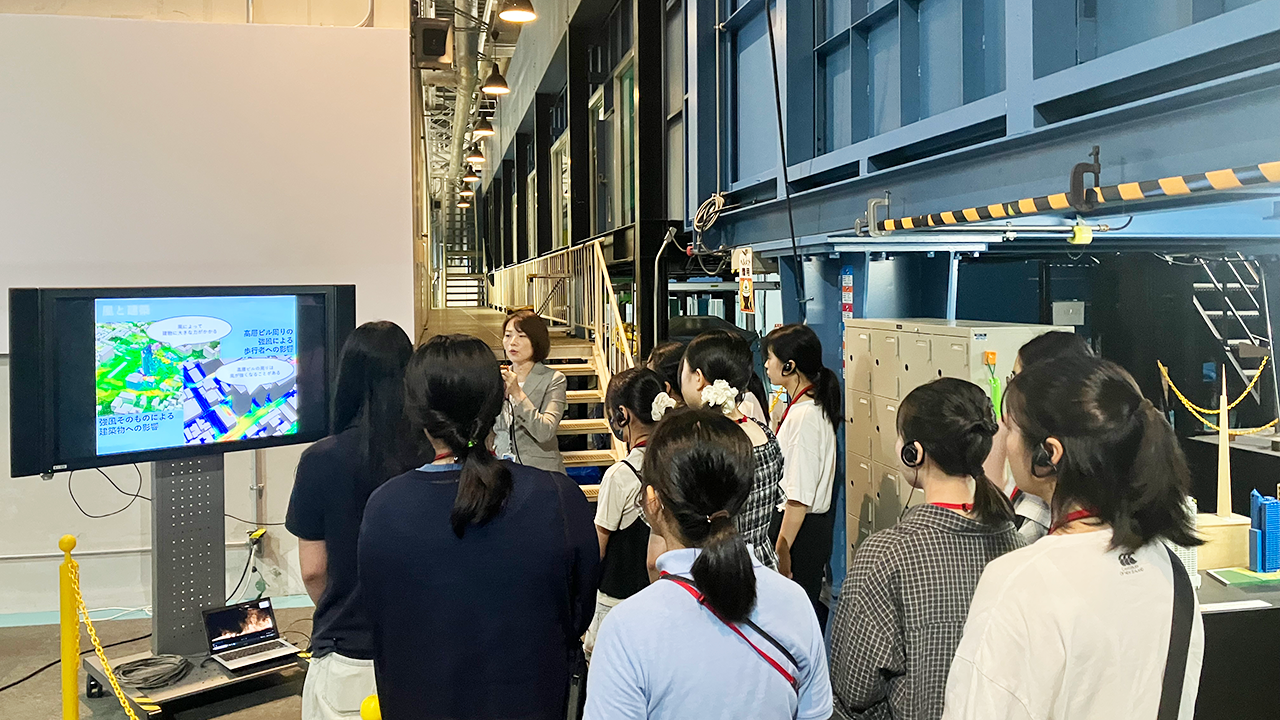 施設見学で、説明を受けながらモニターに表示されたシミュレーション画面を見学する参加者